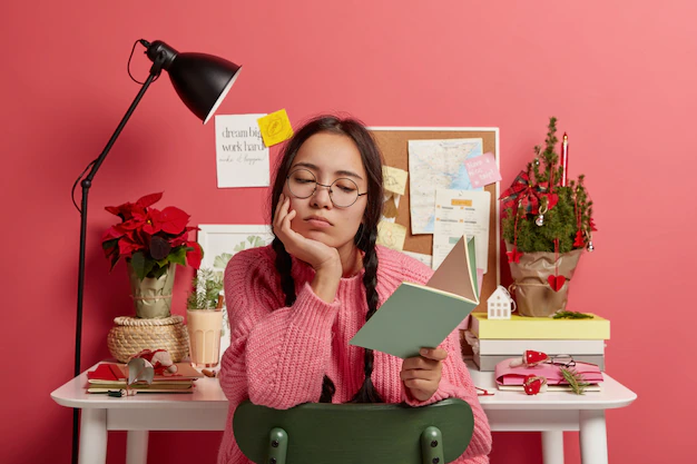 serious-asian-student-learns-information-from-textbook-does-school-homework-wears-round-glasses-sweater-poses-against-desktop_273609-34067